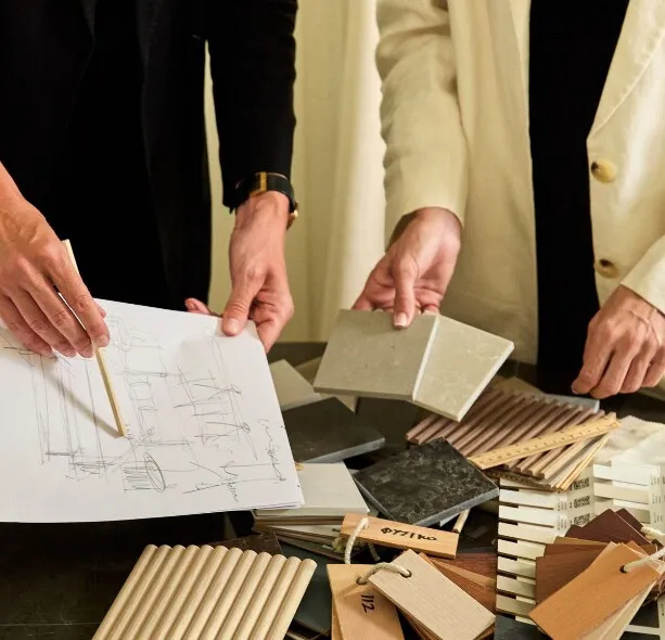 Two people reviewing a sketched floor plan alongside stone and timber material samples