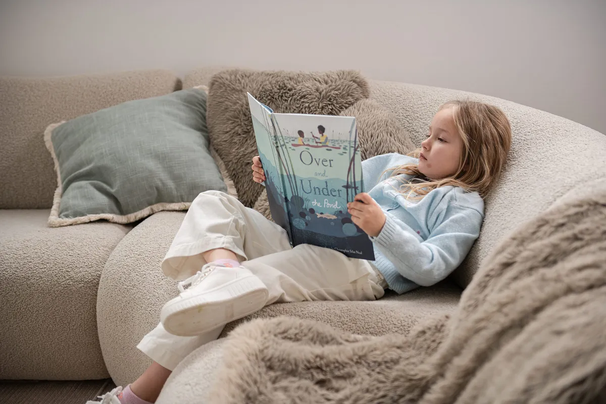 Child reading a picture book on a bouclé sofa in a Dornford custom home living room