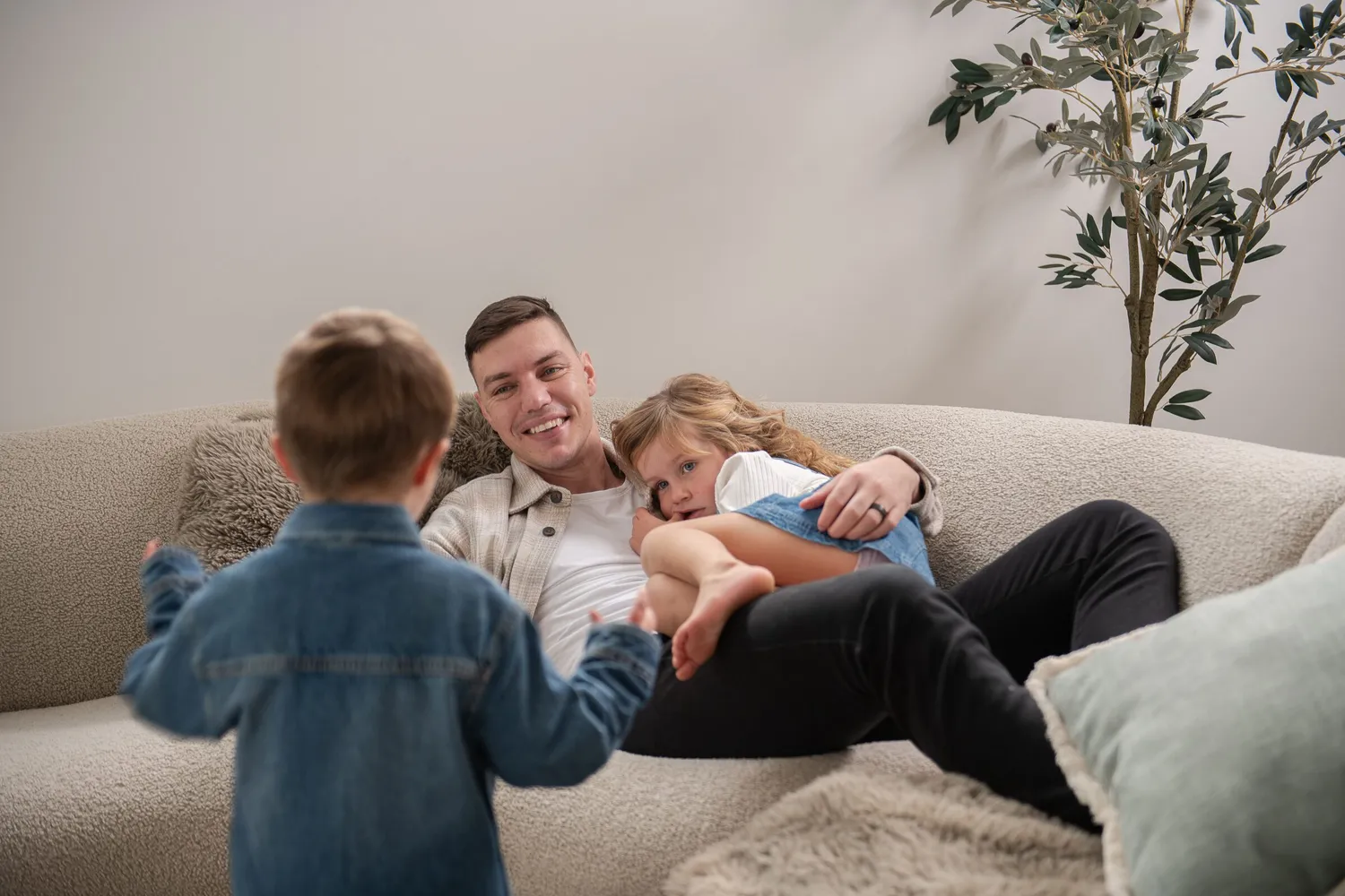 Father and two young children relaxing on the sofa in the living room of a Dornford custom home in Adelaide