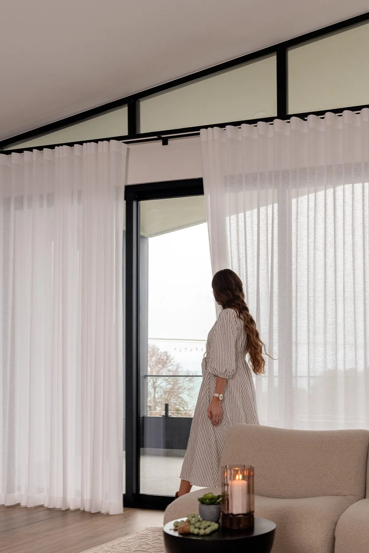 Woman looking out through floor-to-ceiling sheer curtains to the balcony of a Dornford custom home
