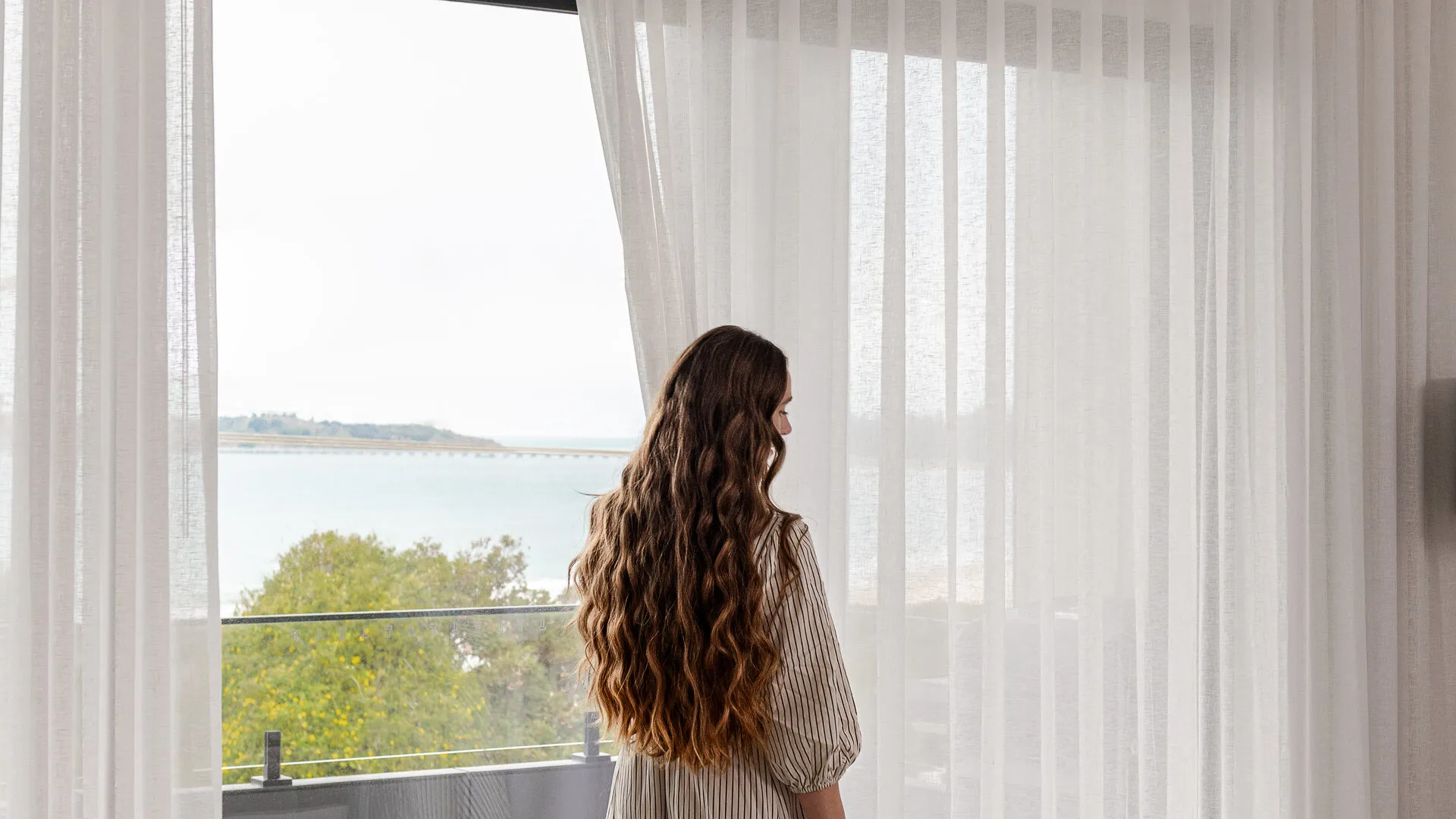 Sheer curtains drawn back from a full-height window in a completed Adelaide custom home, morning light across the living space