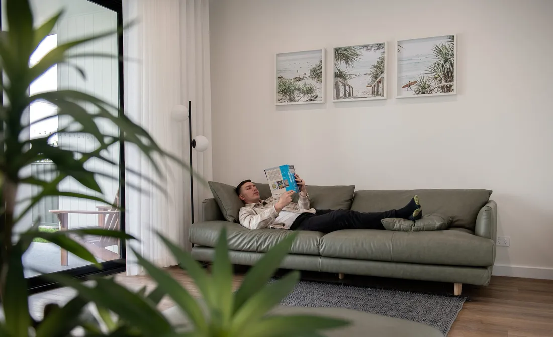 Man reading on a leather sofa beneath a gallery wall of framed beach photographs